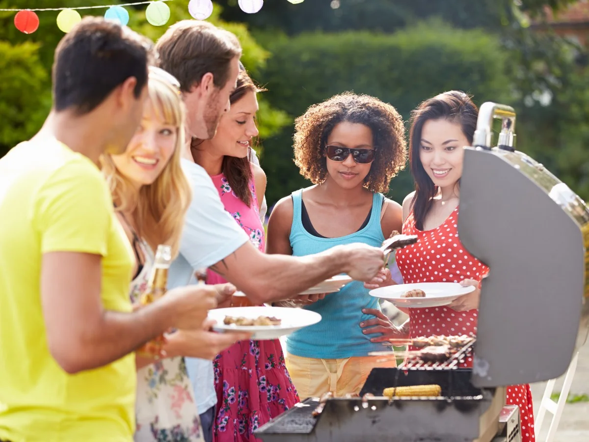 Friends Enjoying BBQ A diverse group of friends enjoying a backyard barbecue, serving food from the grill on a sunny day.